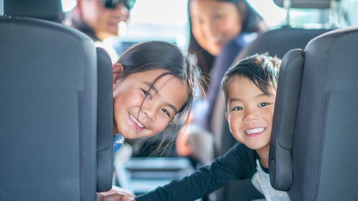 Two kids sitting in the back of a car smiling while their parents look back, too.