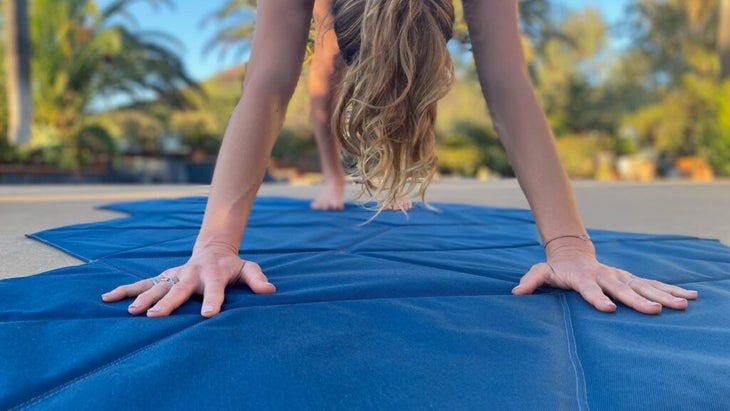 A woman does a downward dog on her foldable Kama Mat.