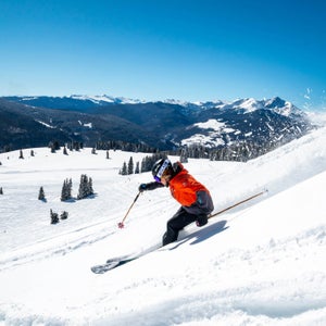 A skier in a red jacket skiing downhill at Vail Resorts on a sunny day