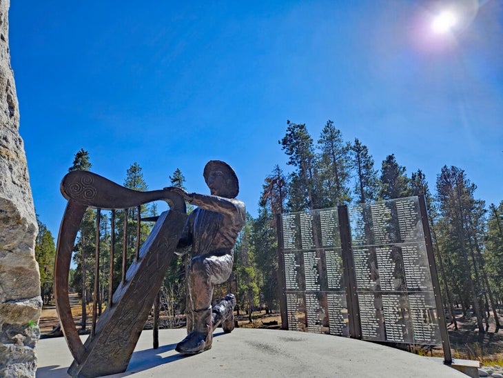 Sculpture of miner with pick axe and harp at a memorial in a pine forest