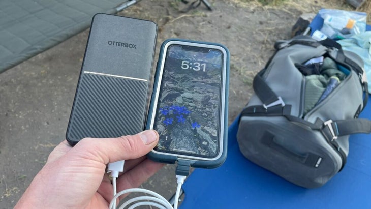 A man holds up his OtterBox Fast Charge next to his cell phone while out on a river trip.