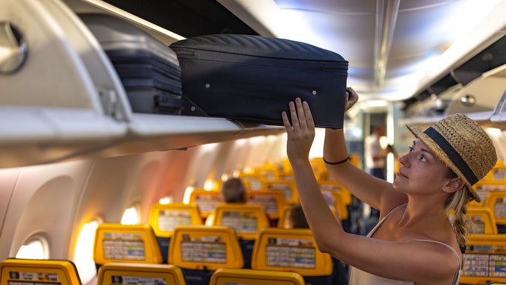 woman putting her carry-on suitcase into an overhead bin on airplane