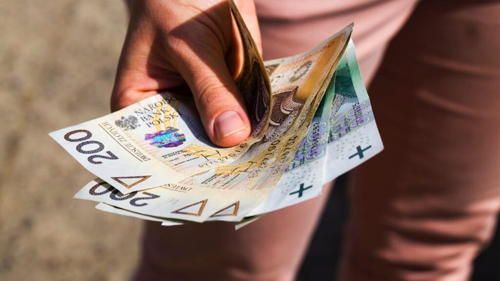 A man holds out several bills of Polish currency.