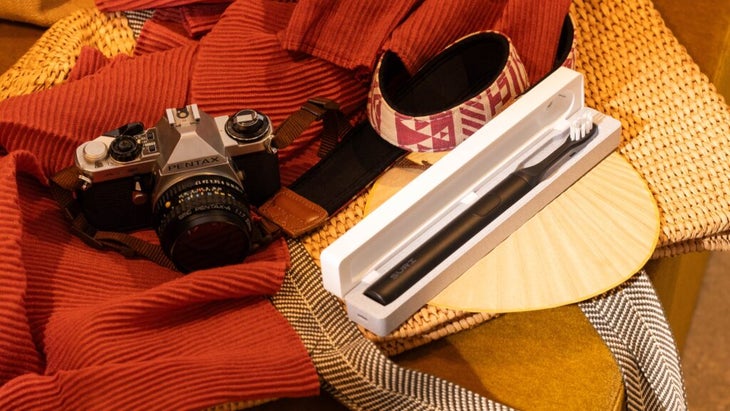 A black Suri electric toothbrush rests in its case next to a camera and sun visor.