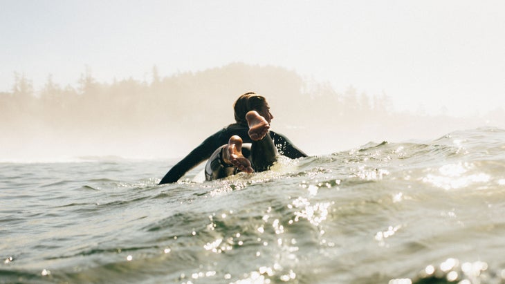 Person on surfboard, paddling in the ocean near tofino