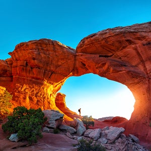 hiker watching sunrise in turret arch, arches national park, utah