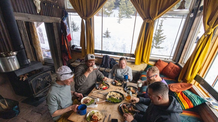 group of adventure travelers sharing a meal in a backcountry colorado hut