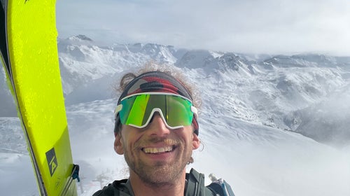 Skier Noah Dines takes a selfie with snow covered peaks in the background