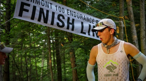 A man in compression sleeves, a tank top, and a baseball cap exhales at the finish line of the Vermont 100 endurance race