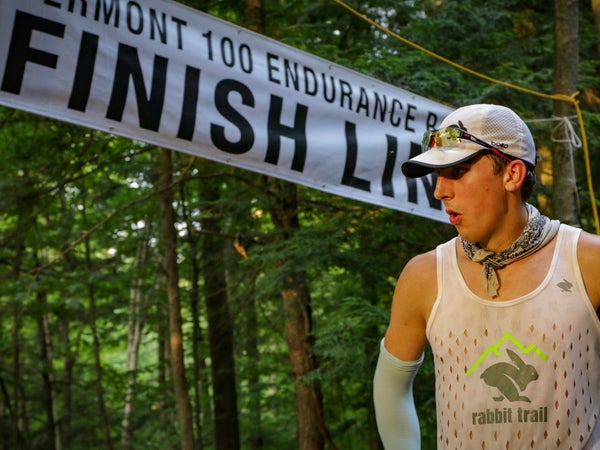 A man in compression sleeves, a tank top, and a baseball cap exhales at the finish line of the Vermont 100 endurance race