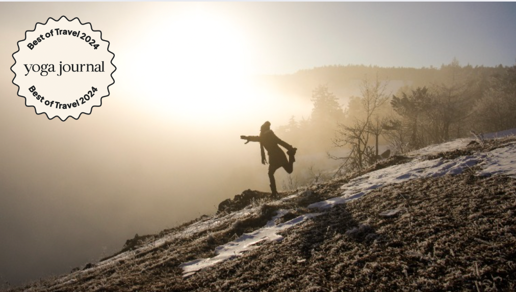 Woman practicing yoga on a snow-covered hill with the Sun going down in the background