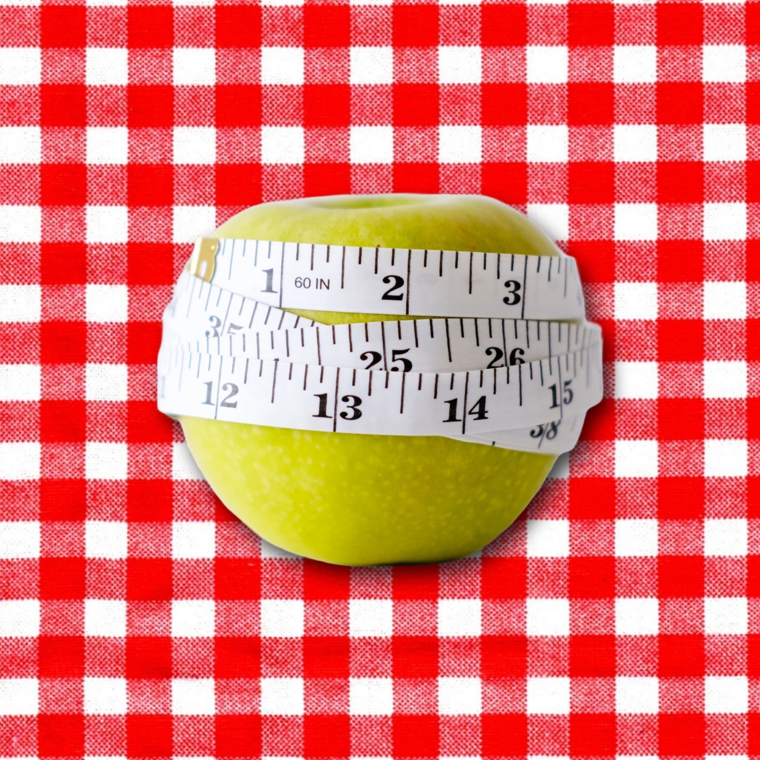 Green apple with white measuring tape wrapped around it on picnic blanket background