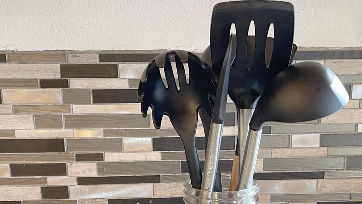 Black plastic kitchen utensils against a tile backsplash