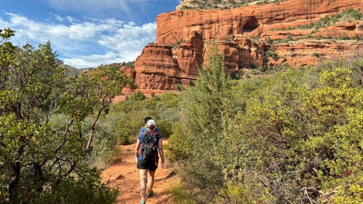 Two women hike a trail amid ponderosa pines and high-desert brush at the base of the Boynton Canyon Trail in Sedona, Arizona.