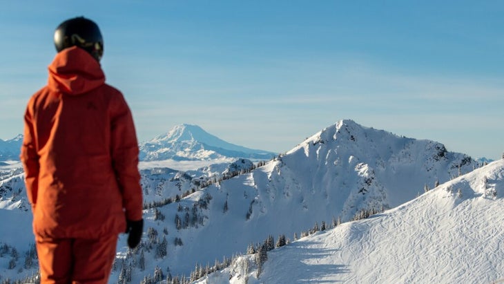 A skier wearing a red kit and a helmet looks over the snow-covered landscape of Crystal Mountain, Washington