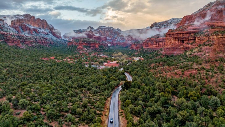 A car drives down the main road away from the Enchantment Resort in Sedona, Arizona. Snow covers the peaks of Boynton Canyon in the background. 