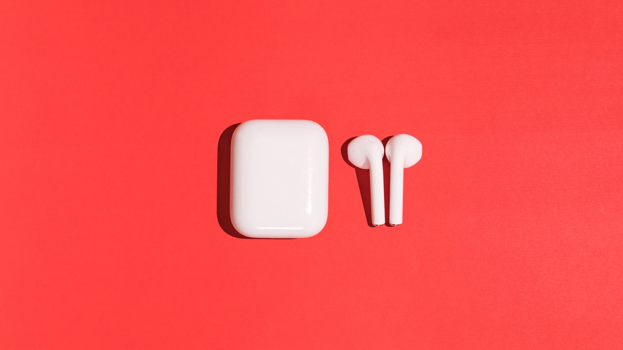Trendy wireless white headphones earbuds on red background.