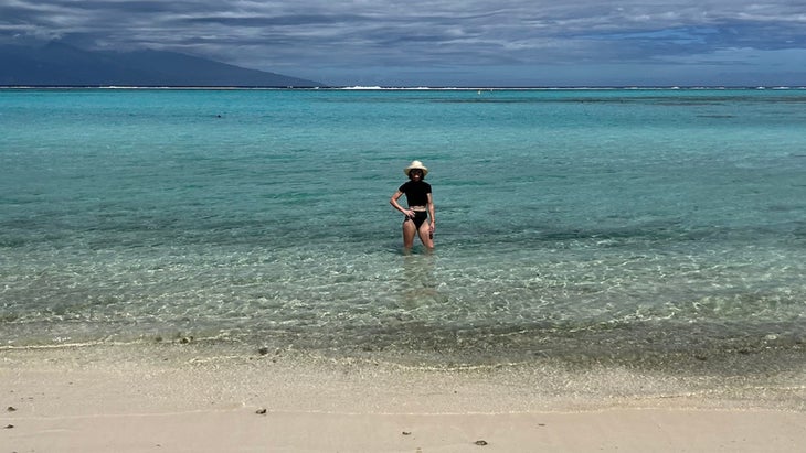 woman wading in clear water in white sands in Moorea