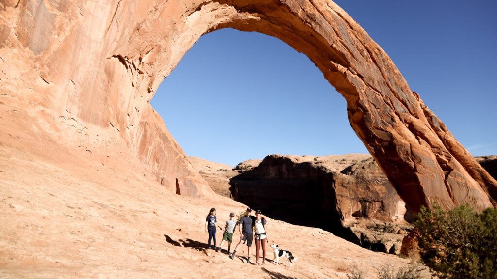 A family of four and their dog pose beneath one of the sandstone arches at Utah’s Arches National Park.