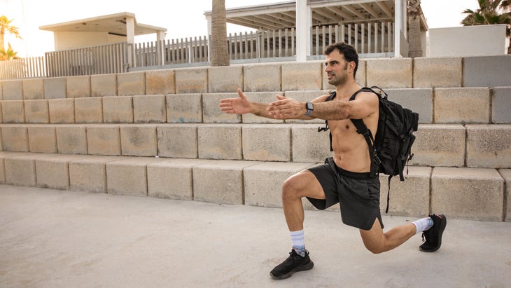 Rucking man lunges while wearing a heavy backpack.