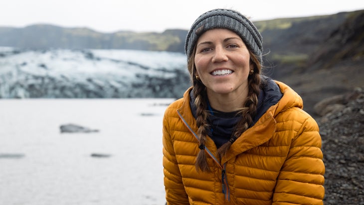 A woman in winter wear poses in Iceland in front of a glacier and iceberg-filled lake.