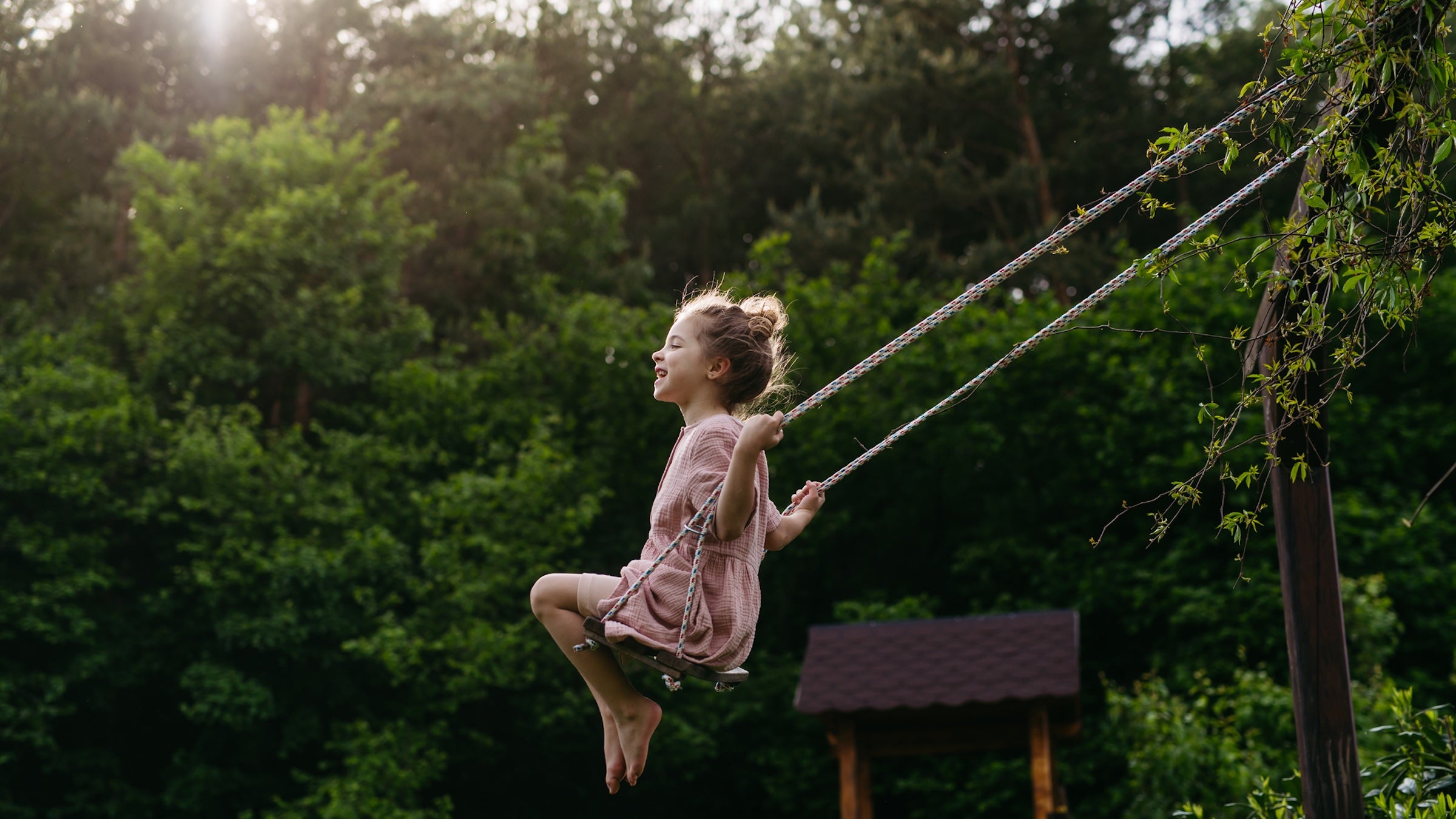 little girl in pink dress swinging high on swing with trees in the background