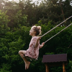 little girl in pink dress swinging high on swing with trees in the background
