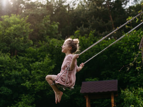 little girl in pink dress swinging high on swing with trees in the background