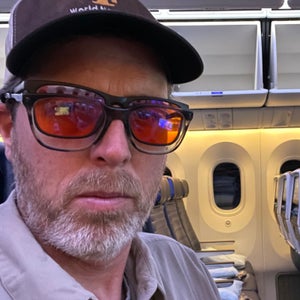 The author sitting in an airplane seat, wearing two pairs of glasses, one of which has orange lenses.