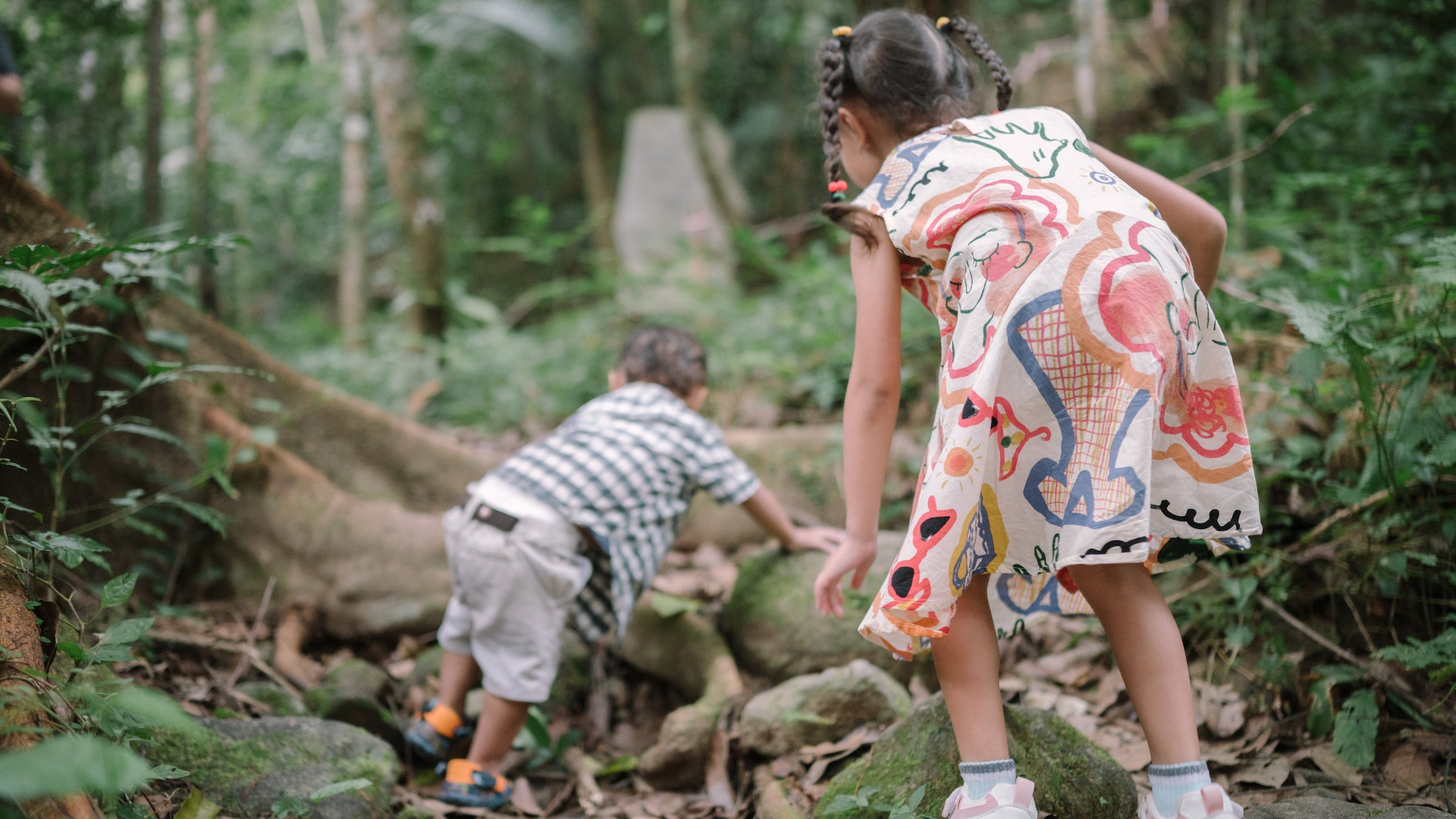 Two children in a forest climb over tree roots