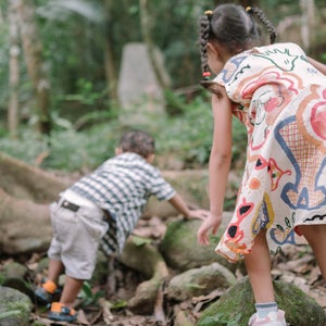 Two children in a forest climb over tree roots