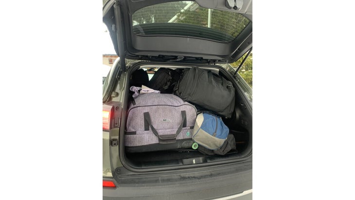 A tiny car with its hatchback popped; it is nearly completely full of various bags. 