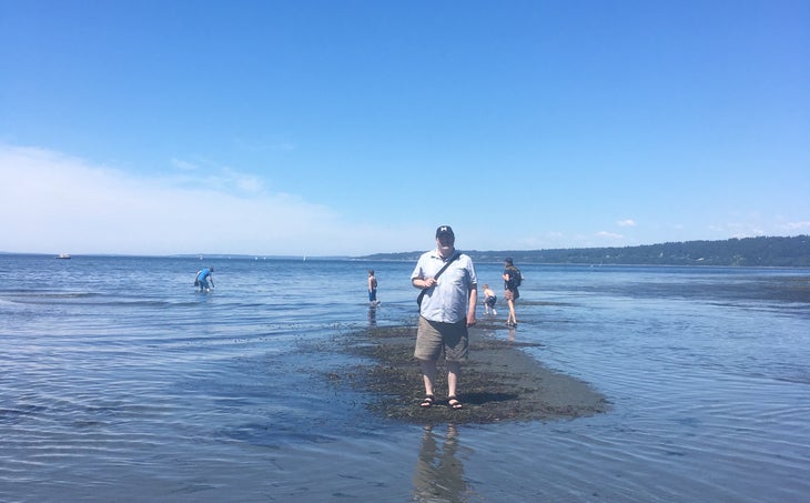 A man stands on a small patch of sand surrounded by water at the beach