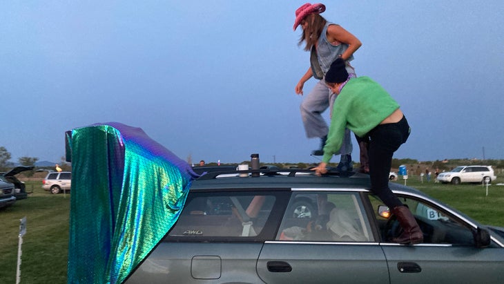 Two people stand on top of a car at dusk