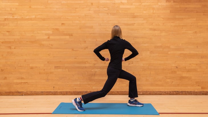 A woman in a gym does a lunge and twists her torso away from the camera