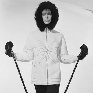 September 1965: A woman in a Gordon Lowe white skiing jacket with a star motif and a black fur hood prepares to set off down the piste