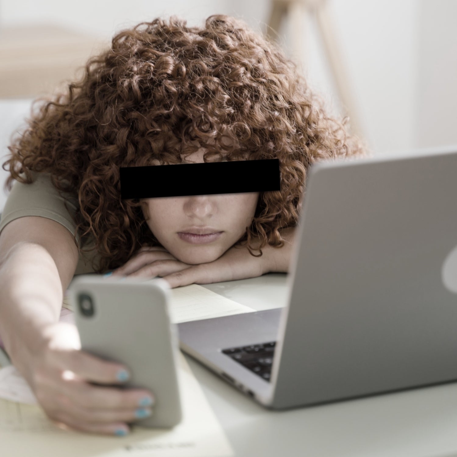 gen z employee scrolls on phone next to open laptop