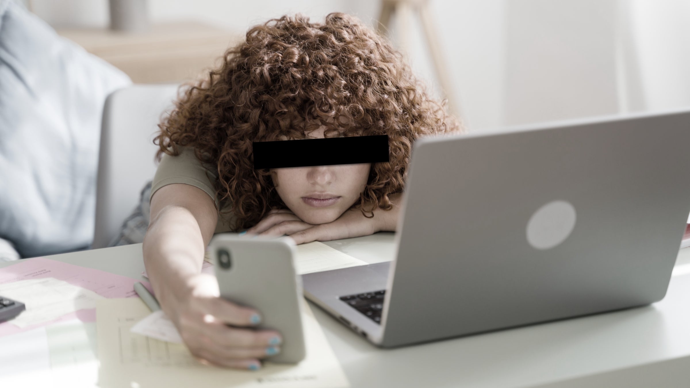 gen z employee scrolls on phone next to open laptop