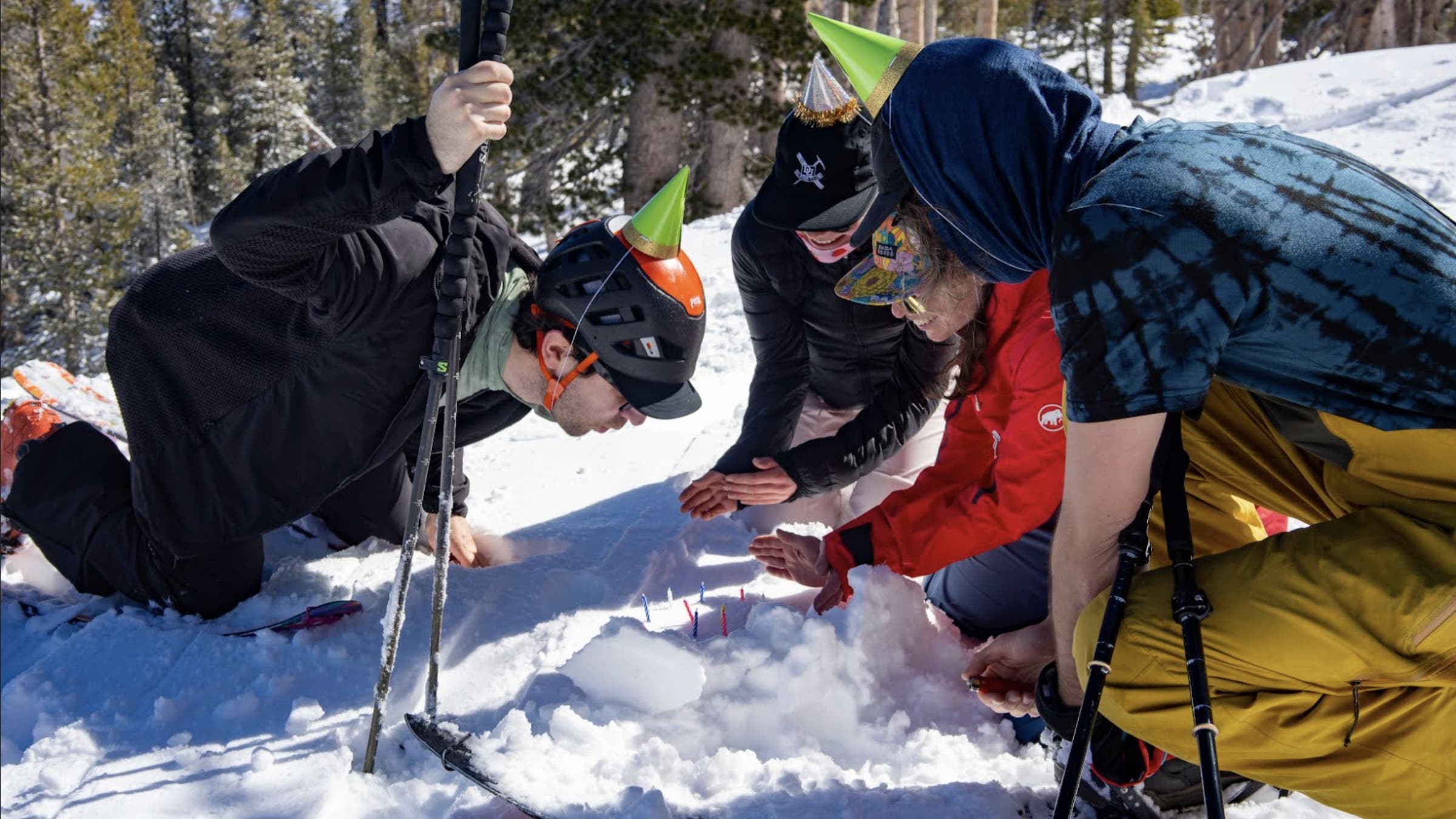 a group of people crouch in the snow around birthday candles. they are wearing birthday hats and have skiing gear with them. skipping new year's resolutions