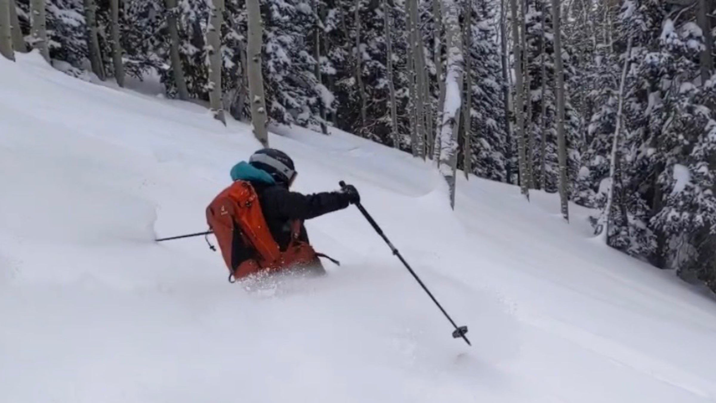 A skier waist-deep in powder shoots down a slope. They are wearing a red backpack and a helmet.