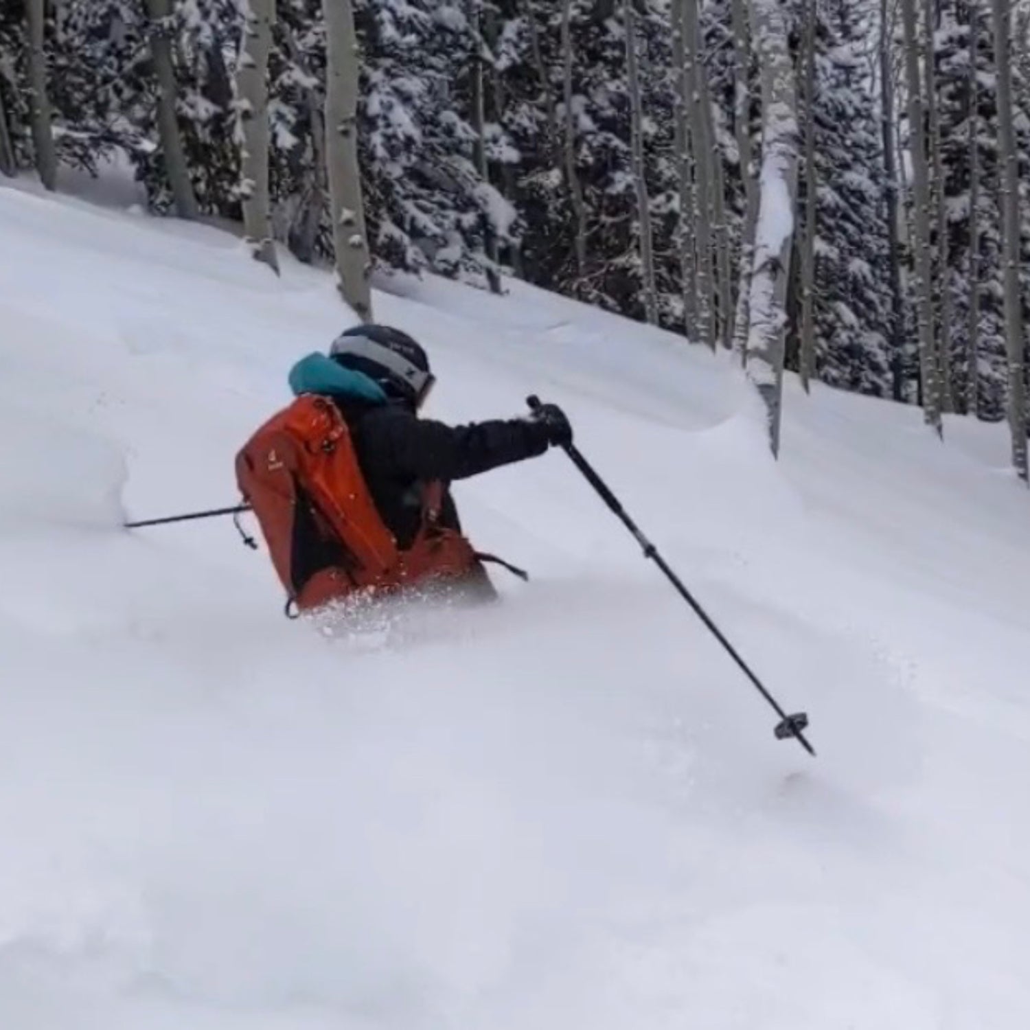 A skier waist-deep in powder shoots down a slope. They are wearing a red backpack and a helmet.