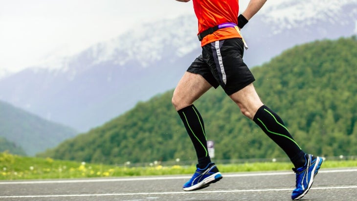 A man running in a mountain setting is seen wearing compression socks