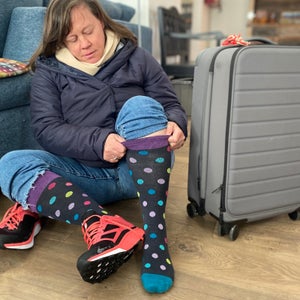 A woman pulls up her polka-dot compression socks while sitting down next to her luggage.