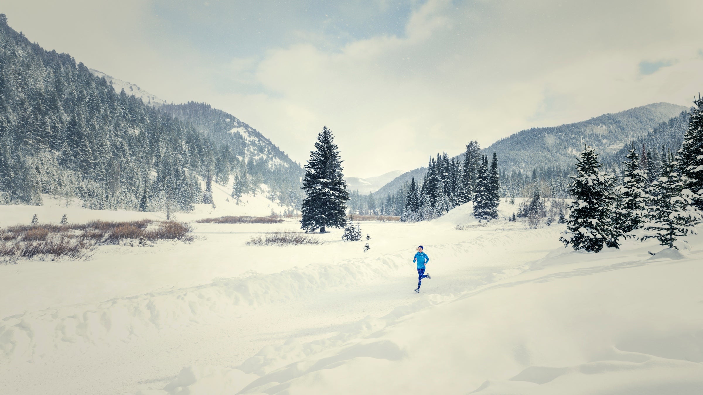 A caucasian woman runs down a plowed road in snowy landscape