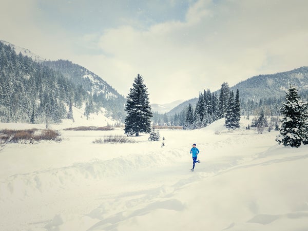 A caucasian woman runs down a plowed road in snowy landscape