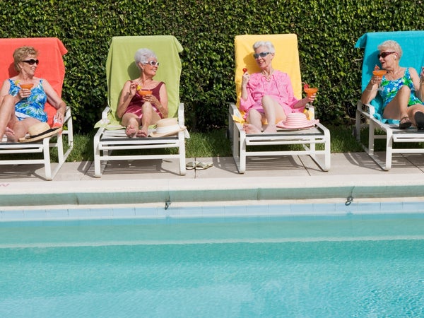 Four elderly women relax by a pool and drink cocktails
