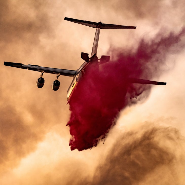 plane dropping red fire retardant in hazy sky