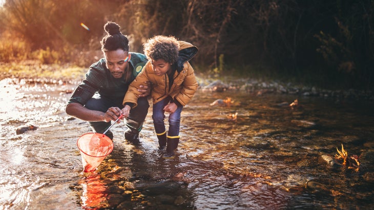 Father-son how to fish with fishing net in mountain stream at sunset