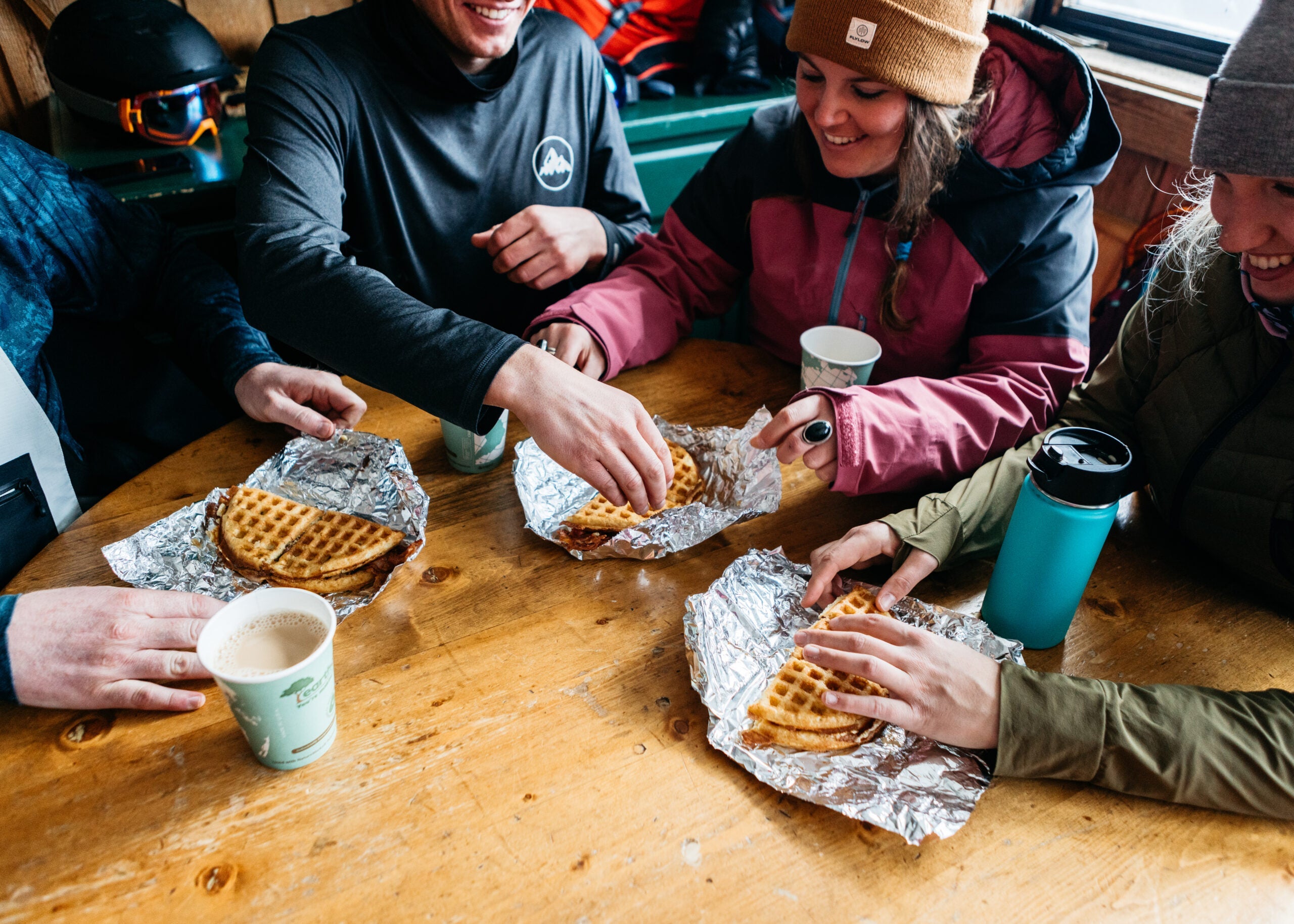 Group of skiers with waffles and coffee on a table.