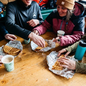 Group of skiers with waffles and coffee on a table.